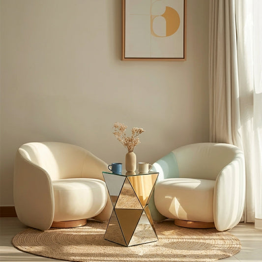 Modern living area with two plush white chairs and a mirrored triangular side table in the center, holding a vase with dried flowers and coffee mugs.