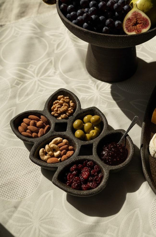 Handmade stoneware serving dish 'PUMPERNICKEL' with compartments containing nuts, olives, and fruit segments.