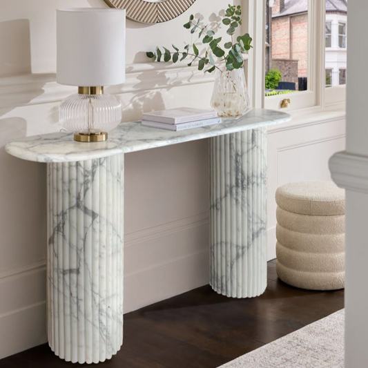 White marble console table with fluted legs against a modern cream wall background.