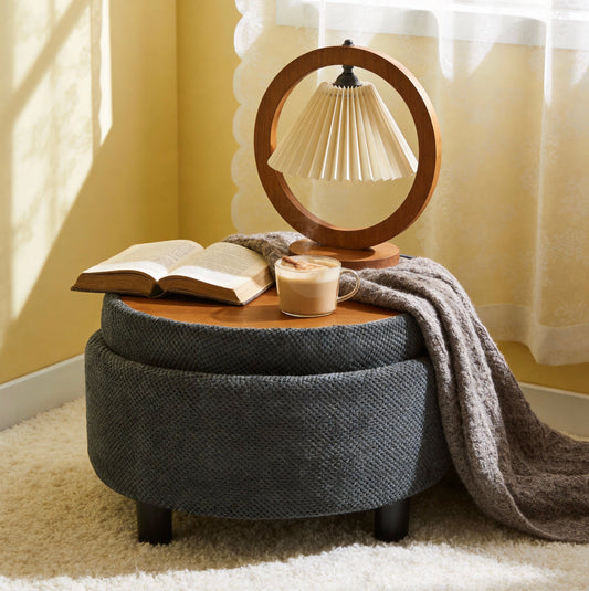 Grey textured fabric ottoman with a round wooden tray holding a cup and book, styled in a cozy reading corner with lace curtains and yellow walls.