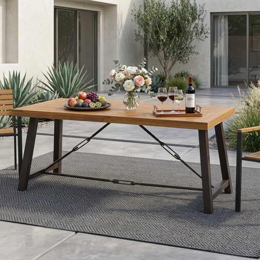 Outdoor dining table with teak wood surface and black metal base, set on a patio with plants and flowers.