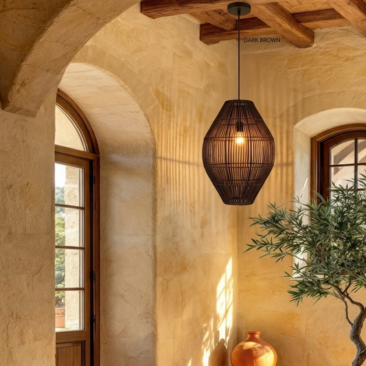 Oval rattan pendant light hanging from a wooden beam; dark brown finish, natural setting with an arched door, window, and decorative vase visible.