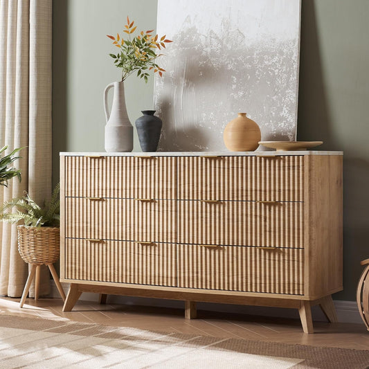 Natural light wood dresser with vertical slats and faux marble top, adorned with various vases and decor, in a cozy living room setting with light green walls and a patterned rug.