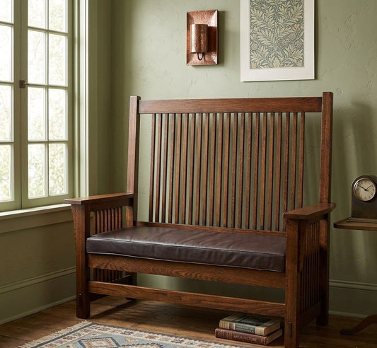 Solid oak bench with spindles, leather seat, set against a green wall near a window, displayed in an upscale homegoods store.