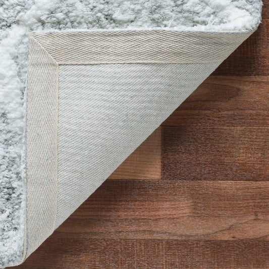 Close-up of a light gray microfiber and cotton shaggy rug on a wooden floor