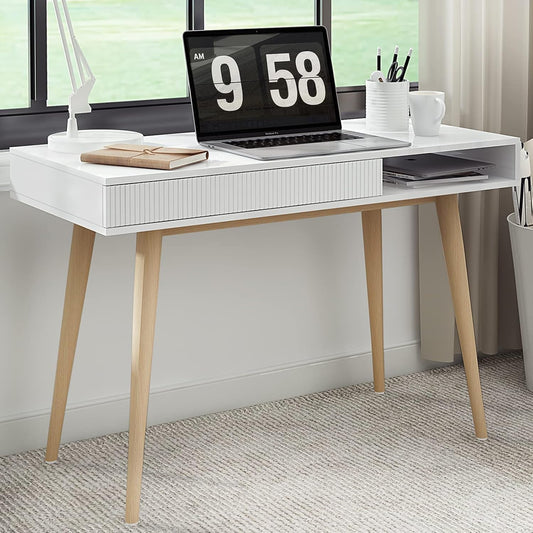 A white desk with a hidden drawer, featuring wooden legs and a minimalist design, set against a window with outdoor greenery and a desk lamp.