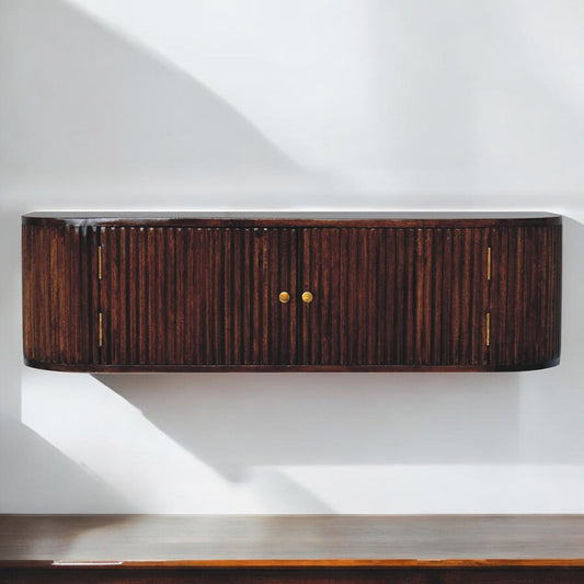A wall-mounted chest with a segmented design, made of dark wood with a glossy finish and brass hardware, positioned above a reflective wood surface against a plain white wall.
