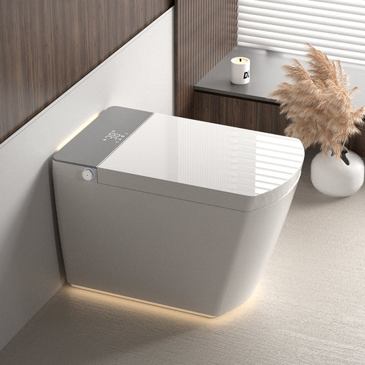 A modern integrated smart toilet with light grey and white surfaces. Setting shows a minimalist bathroom with wooden paneling and decorative elements on a side table.