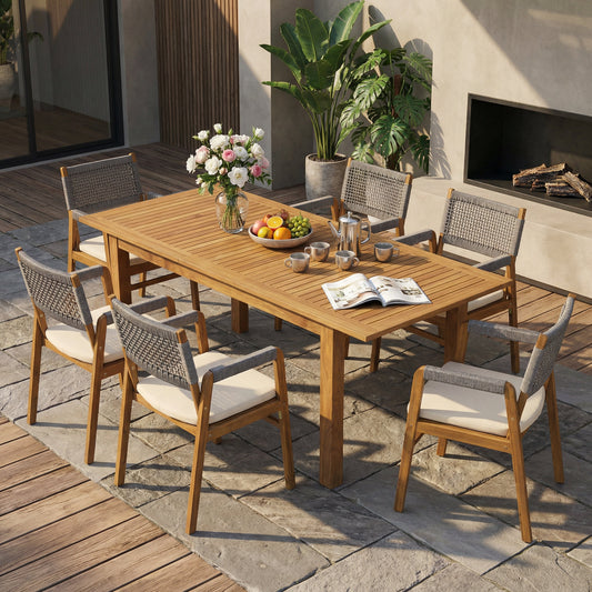 Outdoor 7-piece Acacia expandable dining set with cushions, on a patio with plants and a fireplace, sunlit setting.