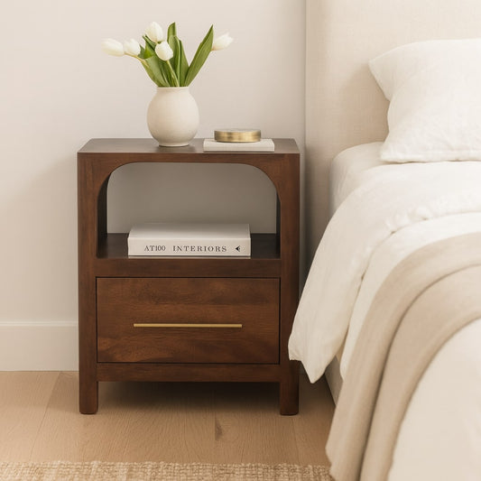 Brown solid wood arc-line bedside table with books and a vase of tulips on it, next to a bed with white bedding.