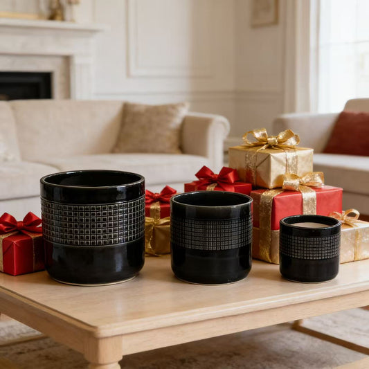 Three handcrafted black ceramic pots with texture on a table with wrapped gifts, in a neatly arranged living space