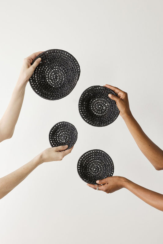 Black hand-woven nested baskets in hands against a plain white background