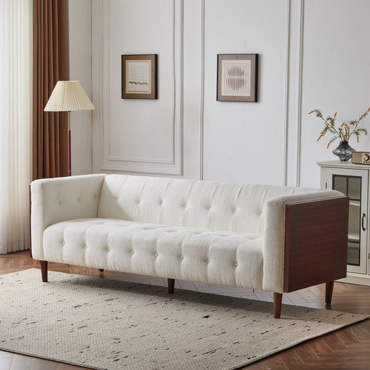 3-seater sofa with tufted cream upholstery and wooden legs, placed in a room with white walls and framed artwork.