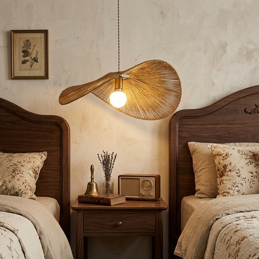 A pendant lamp with a natural rattan design suspended above a wooden nightstand with vintage items, in a bedroom setting.