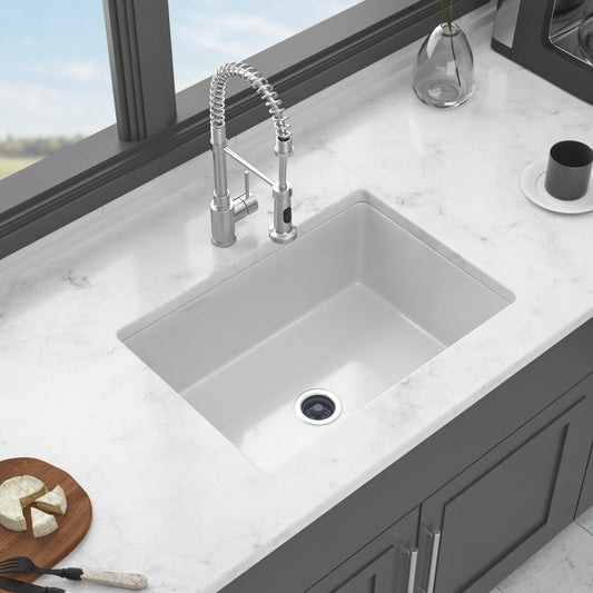 White fireclay undermount single sink with stainless steel faucet on marble countertop, surrounded by kitchen items.