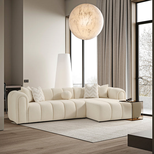 A cream tufted sectional sofa in a modern living room with large windows, a spherical hanging light, and minimal decor.