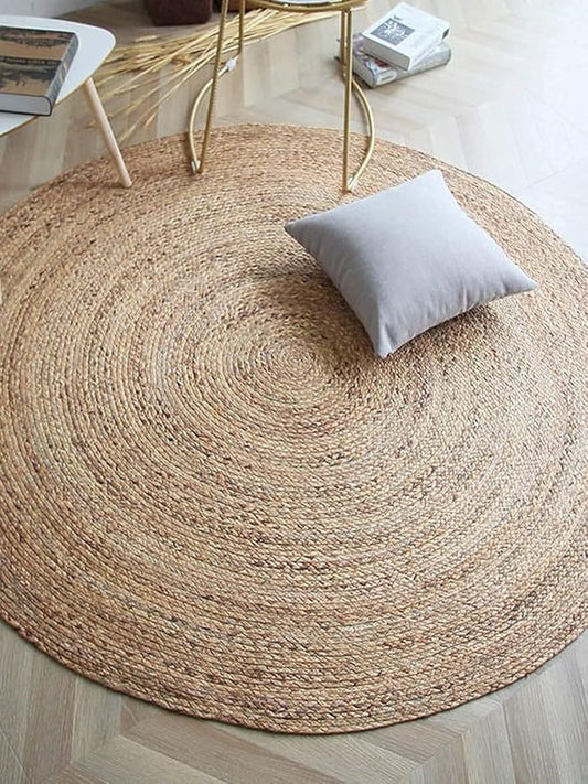 Handwoven Jute Round Area Rug Carpet with natural fibers and reversible design, placed on a light wooden floor, complemented by a cushion.