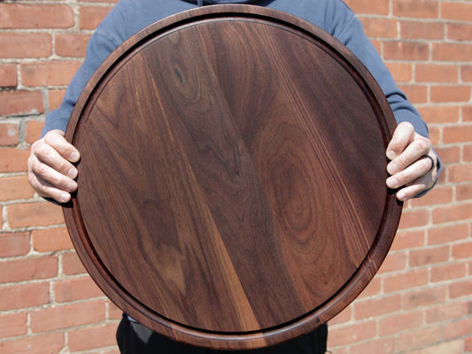 Person holds brown walnut cheese board.