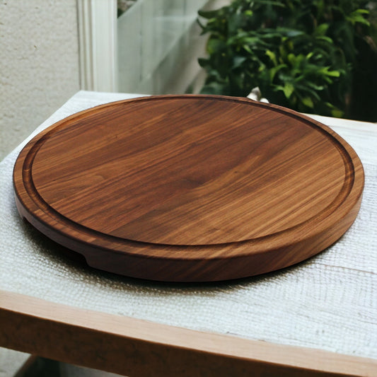 Extra large round wooden cutting board with feet and pocket handles, placed on textured fabric with a plant in the background.