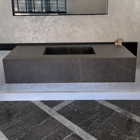 Modern kitchen sink with grey engineered stone construction, infinity design, mounted on the wall with a black and white tile patterned floor and a textured wall in the background,