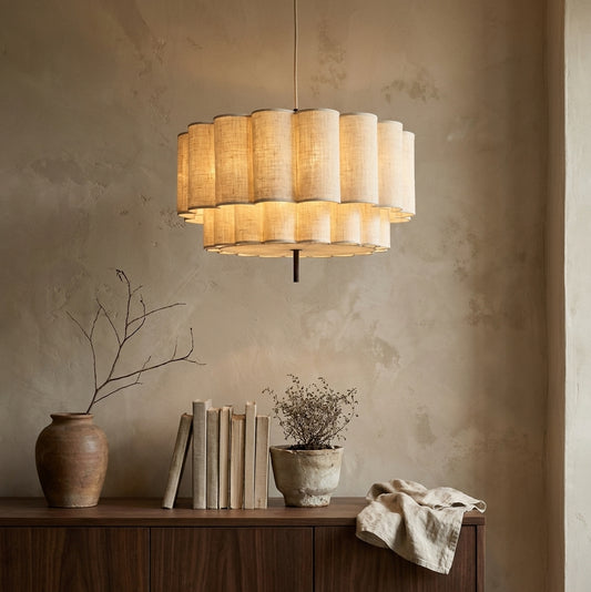 A lit modern pendant light with layered cylindrical shades hanging above a wooden shelf,