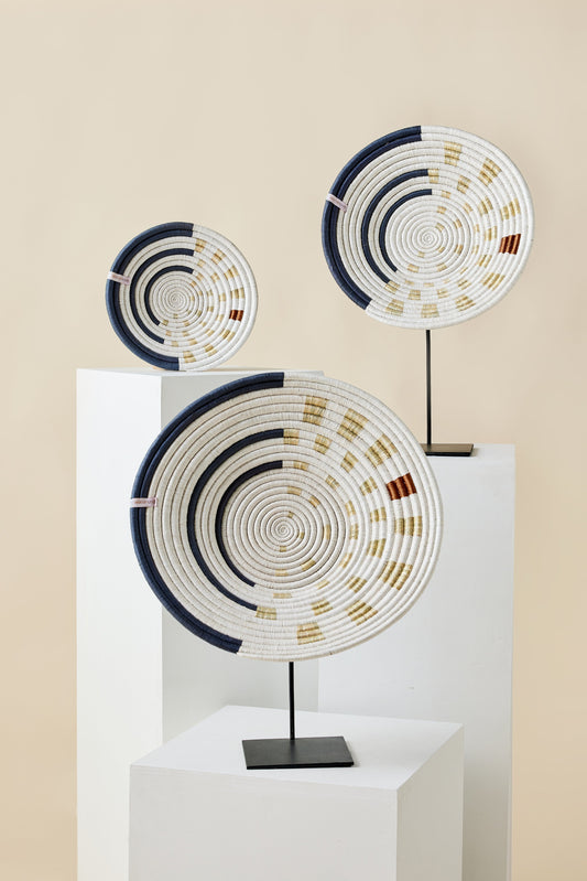 Three large spiral wall baskets with navy, cream, and gold patterns displayed on white stands against a neutral background.