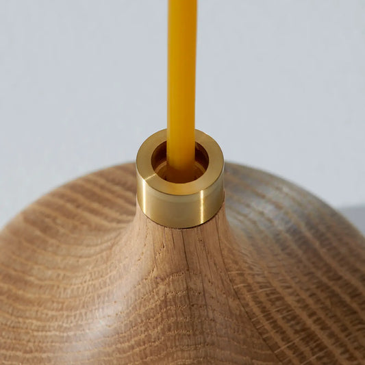Wooden candle holder with a brass ring, yellow candle, light background.