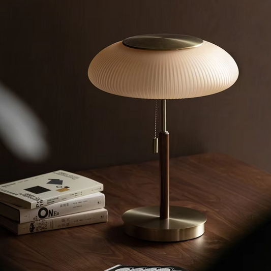 Vintage brass desk lamp with pleated glass shade on a wooden table, stacked books nearby