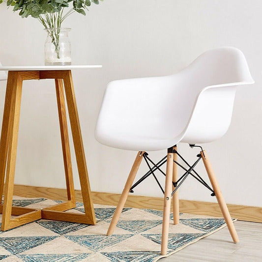 Two white modern molded armchairs with wooden legs, placed next to a wooden table with a vase of plants on it.