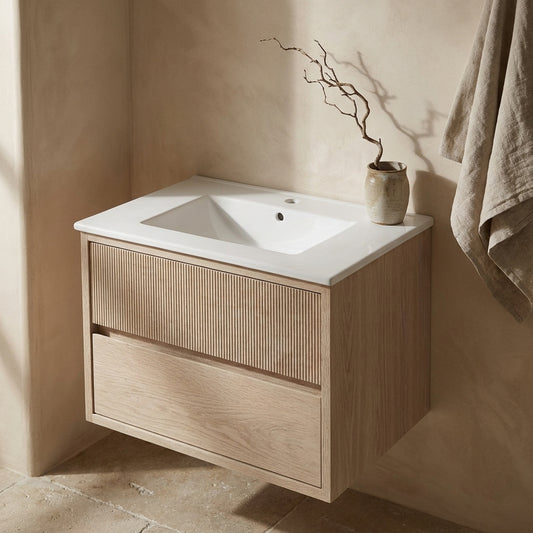 Modern wooden bathroom vanity with ceramic top, beige walls, and a decorative branch in a vase.