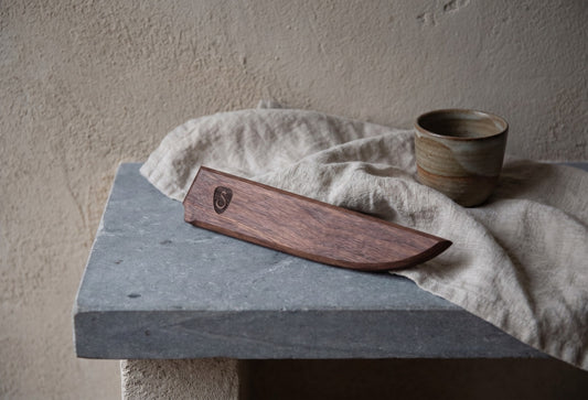 A wooden knife sheath with a smooth finish placed on a stone surface.
