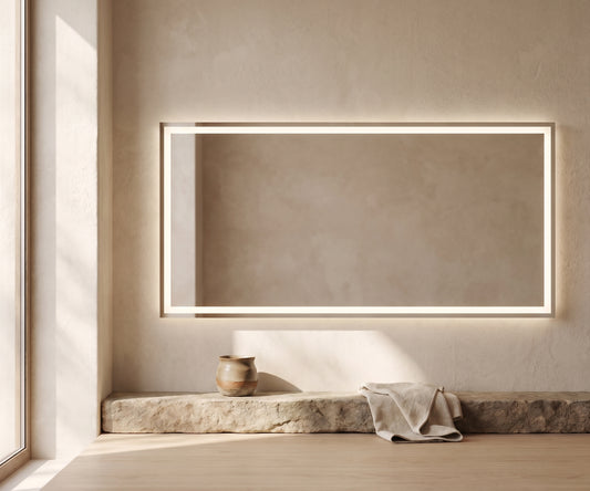 Large rectangular LED mirror with frosted glass frame, mounted on textured wall above stone bench with towel and vase.