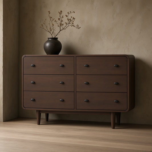 Dark brown dresser with simple design, small black vase with dried flowers on top on a hardwood floor against a textured wall.