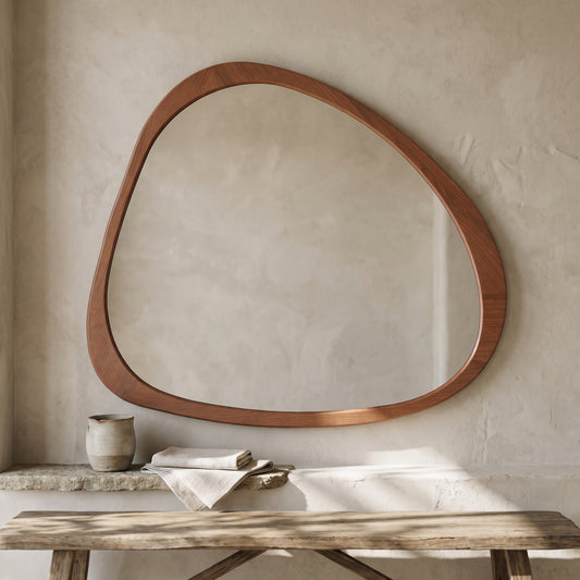 Asymmetrical wall mirror with natural wood frame, placed in a minimalist interior with textures and a table in front.