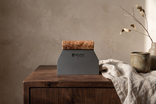 A bench scraper with dark metal and wood top placed on a wooden table.