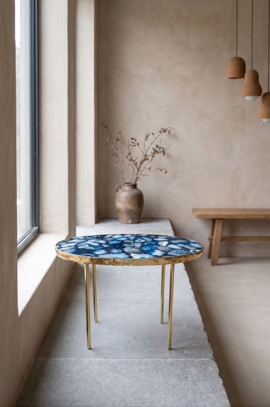 Blue Oval table with agate and crystal inlay, gold edge, on thin legs, in minimalist room with windows and simple decor.