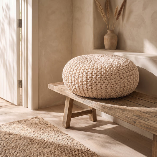 A woven beige pouffe on a wooden bench in a rustic setting