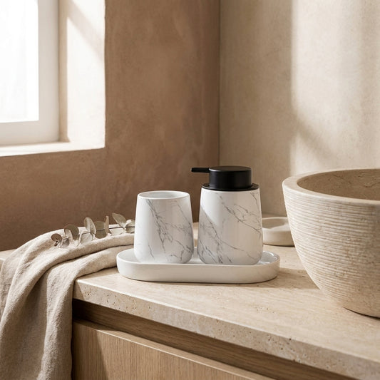 White marble-patterned ceramic bathroom set on a white tray, with a black faucet and sink in the background, natural window light, beige walls, beige towel, and olive branches.