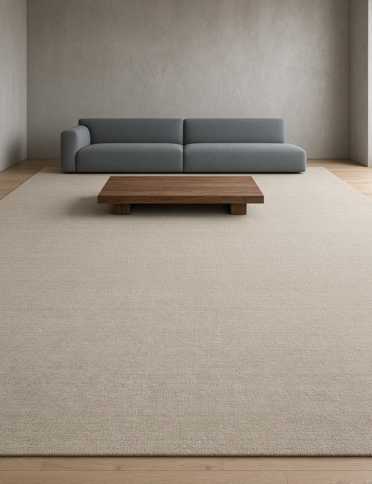 Beige hand knotted rug covering the floor in a room with a modern sofa and wooden table, neutral walls and light wood flooring.