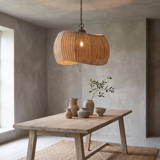 Curved wicker pendant light above wooden table with ceramic vases and plant.