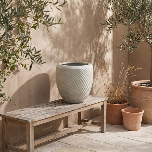 White textured planter on wooden bench with terracotta pots and olive tree in rustic setting
