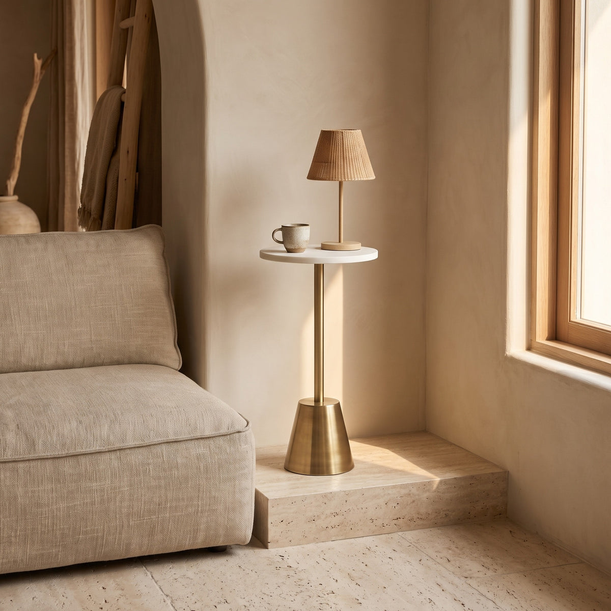 Minimalist Crane martini table with brass base and marble top in an elegant living room setting, next to a beige sofa and large window, featuring soft natural lighting.