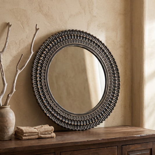 Black and gold round wooden accent mirror with woven texture, displayed on a wooden console table in a minimalist setting.