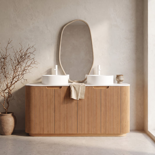 A wooden vanity with oval sinks and a textured stone top, mounted on the wall above two small sinks, with an abstract mirror above and a beige towel draped on the front, set against a plain wall in a minimalistic bathroom with a potted plant beside it.