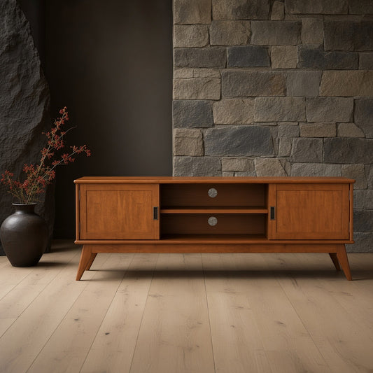 A 72-inch wooden TV stand with a teak finish against a stone wall, placed on a hardwood floor next to a pottery vase with red stems.
