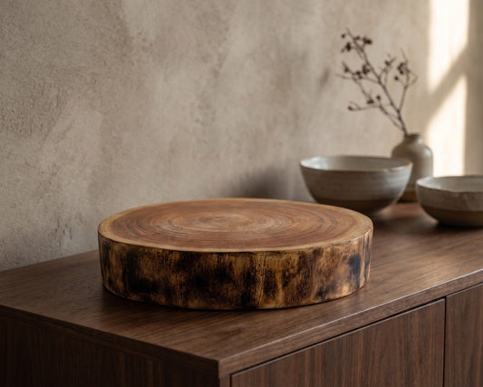 Round wooden cutting board with tree trunk rings, placed on a wooden table in a rustic setting.