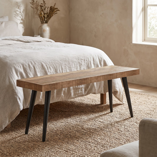 A distressed Durham 43 Inch Wide Solid Mango Wood Bench with black metal legs, placed in a neutral bedroom setting