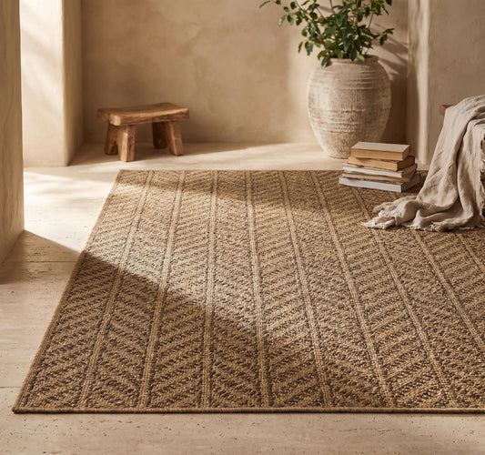 An indoor/outdoor area rug with a simple geometric pattern on a natural fiber background, placed on a concrete floor.