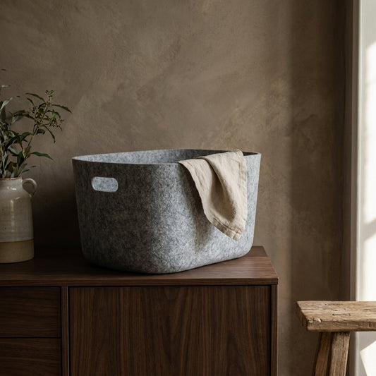 Fuzzy gray storage bin with fabric handles on wooden cabinet, beige wall background, green plant.
