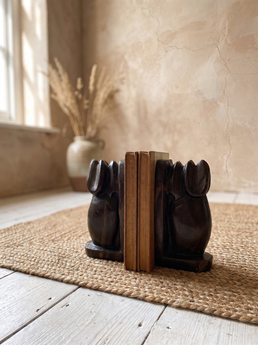 Dark brown elephant-shaped stone bookends holding a pair of books, placed on a woven mat.
